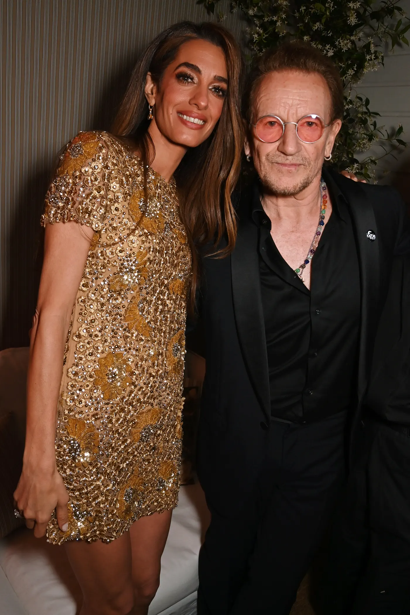 Amal Clooney wears a gold dress adorned with flowers, sequins, and diamonds, as she poses with Bono at Cannes Film Festival 2025