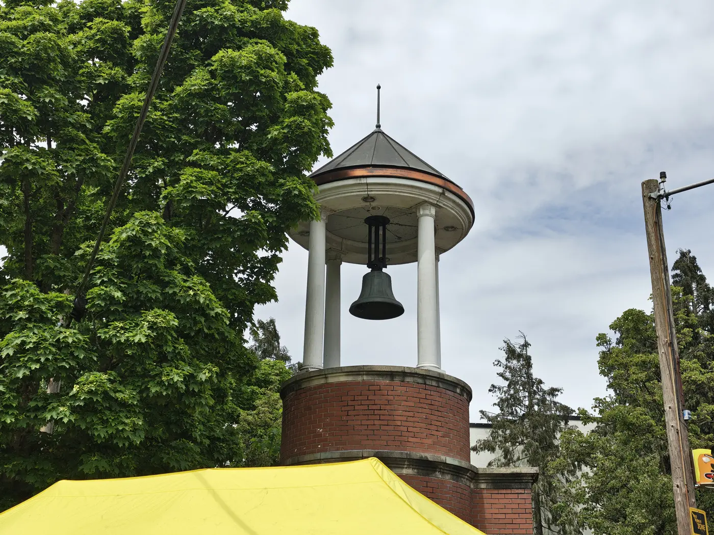 A bell tower next to a tree and a yellow tend