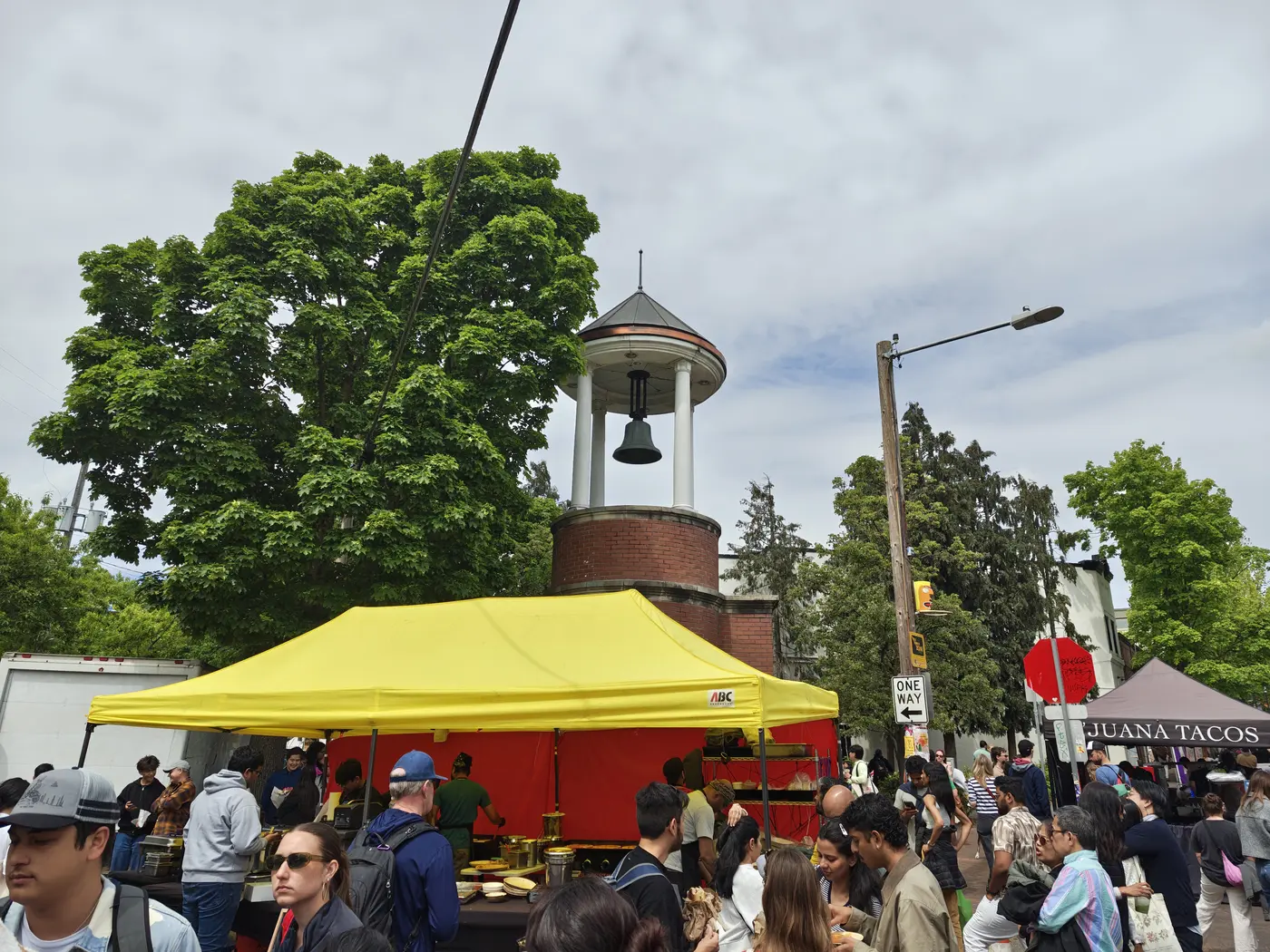 A bell tower next to a tree with people walking underneath