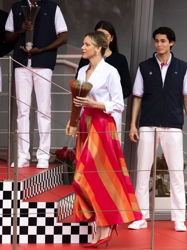 Princess Charlene in a striped skirt and white shirt holding flowers