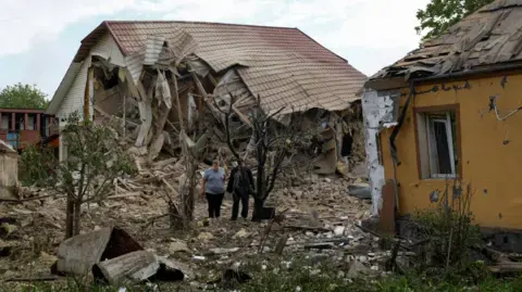 Reuters Two men stand next to their homes which were struck by a Russian drone in an attack outside of Kyiv on 18/5/2025
